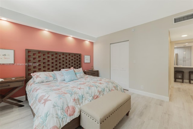 bedroom with visible vents, a closet, baseboards, light wood-style flooring, and stainless steel refrigerator