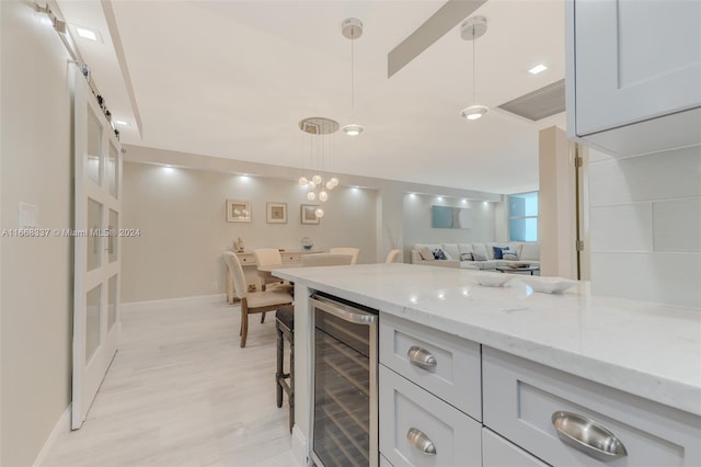 kitchen with wine cooler, a barn door, light hardwood / wood-style flooring, decorative light fixtures, and light stone countertops