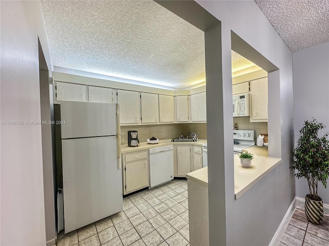 kitchen featuring sink, white appliances, a textured ceiling, cream cabinetry, and backsplash