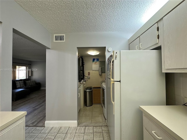 kitchen featuring a textured ceiling, light wood-type flooring, white fridge, and tile walls