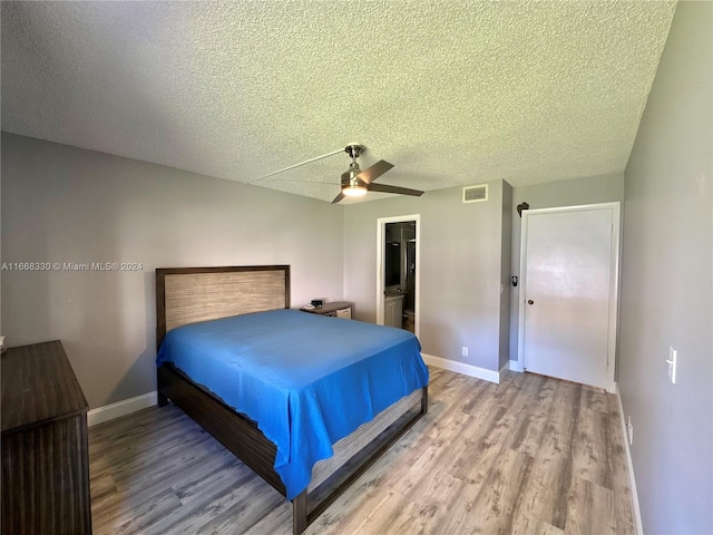 bedroom featuring a closet, a textured ceiling, light hardwood / wood-style flooring, a spacious closet, and ceiling fan