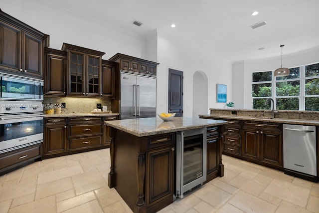 kitchen featuring built in appliances, hanging light fixtures, backsplash, dark brown cabinetry, and beverage cooler