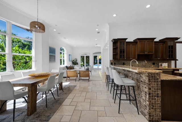 kitchen featuring backsplash, a wealth of natural light, light stone counters, and decorative light fixtures