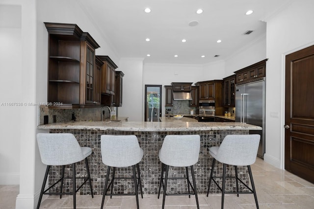 kitchen with kitchen peninsula, ornamental molding, dark brown cabinets, and built in refrigerator