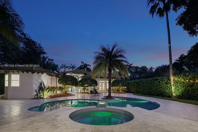 pool at dusk with an in ground hot tub and a patio area