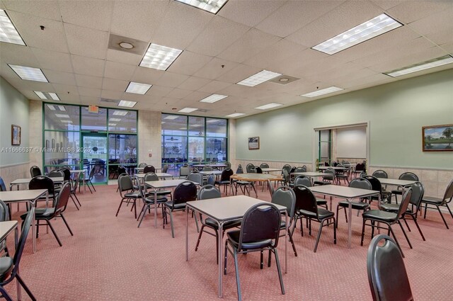 carpeted dining room featuring a drop ceiling and a wall of windows