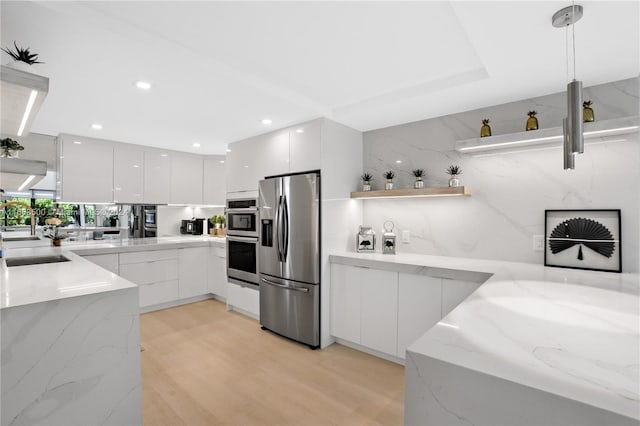 kitchen with light stone counters, white cabinets, hanging light fixtures, sink, and stainless steel appliances