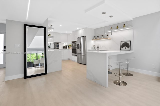 kitchen featuring a breakfast bar area, decorative light fixtures, kitchen peninsula, white cabinets, and appliances with stainless steel finishes