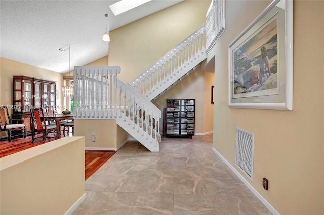 stairway featuring a chandelier, a textured ceiling, high vaulted ceiling, and a skylight