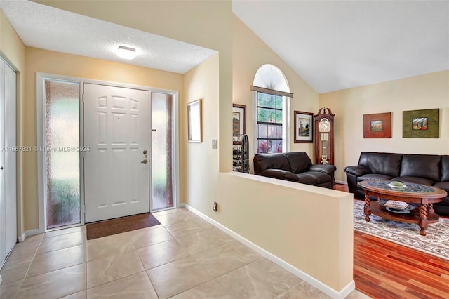 entryway with a textured ceiling, light hardwood / wood-style flooring, and vaulted ceiling