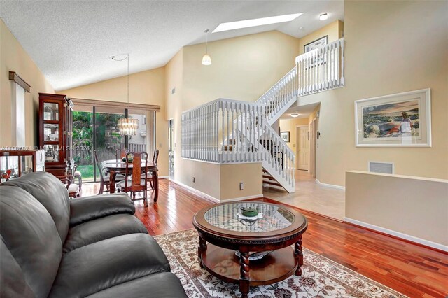 living room with a skylight, a textured ceiling, wood-type flooring, high vaulted ceiling, and a notable chandelier