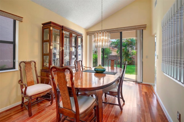 dining space with a textured ceiling, wood-type flooring, vaulted ceiling, and a notable chandelier