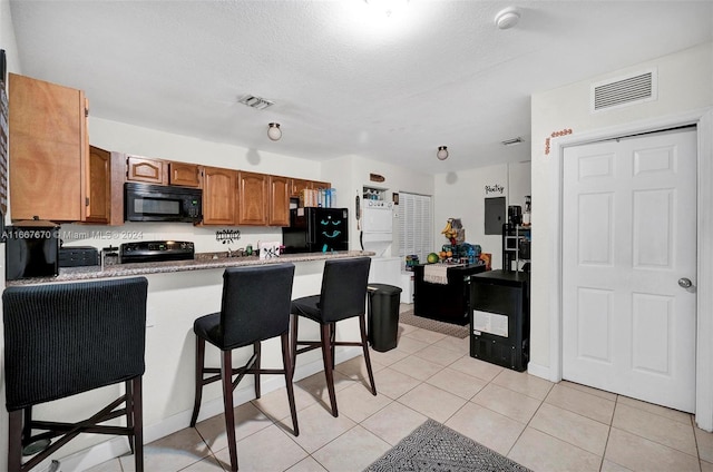 kitchen featuring light tile patterned floors, kitchen peninsula, a textured ceiling, black appliances, and a kitchen breakfast bar