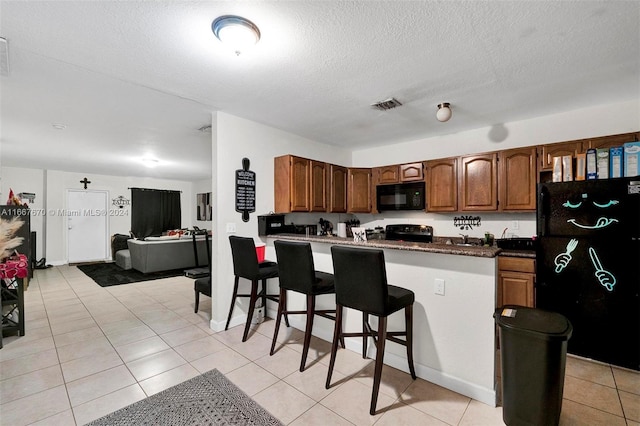 kitchen with kitchen peninsula, light tile patterned floors, a textured ceiling, black appliances, and a kitchen bar