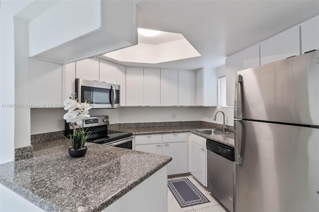 kitchen with white cabinets, sink, light tile patterned floors, appliances with stainless steel finishes, and kitchen peninsula