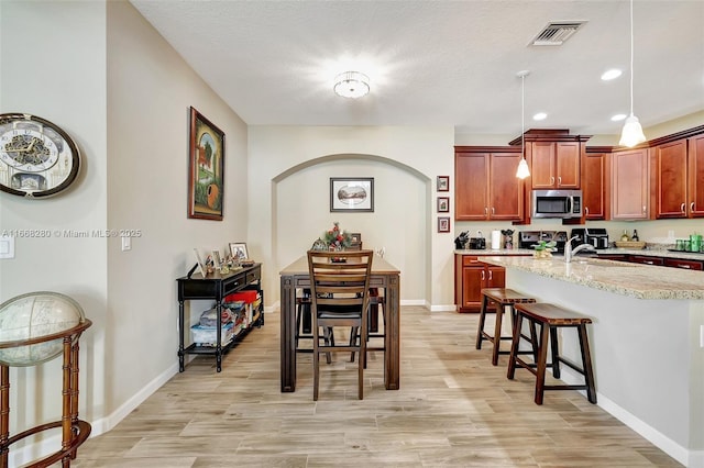 kitchen featuring sink, light stone counters, decorative light fixtures, electric range oven, and a kitchen bar