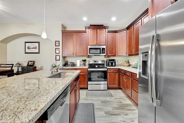 kitchen featuring light stone countertops, sink, light hardwood / wood-style flooring, decorative light fixtures, and appliances with stainless steel finishes