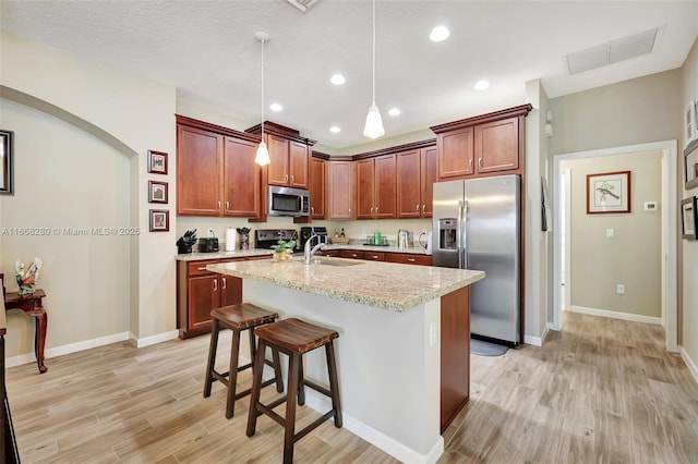 kitchen featuring appliances with stainless steel finishes, light stone counters, sink, decorative light fixtures, and light hardwood / wood-style floors