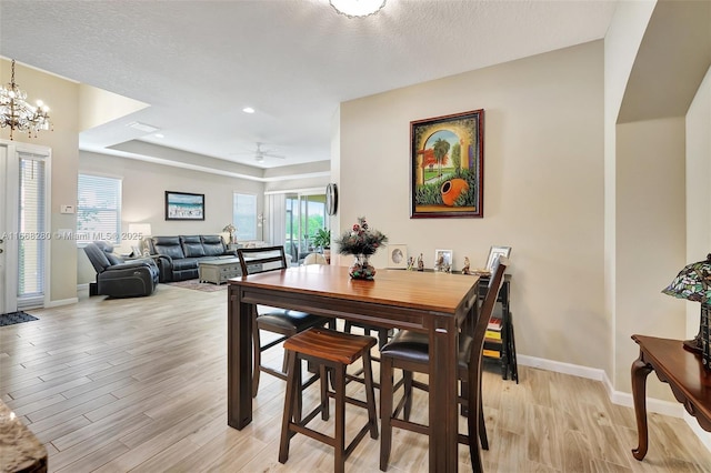 dining space featuring a textured ceiling, ceiling fan with notable chandelier, light hardwood / wood-style floors, and a healthy amount of sunlight