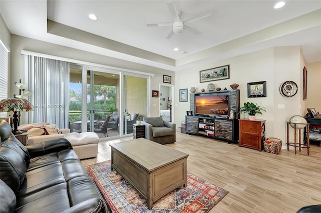 living room featuring light wood-type flooring, a tray ceiling, and ceiling fan