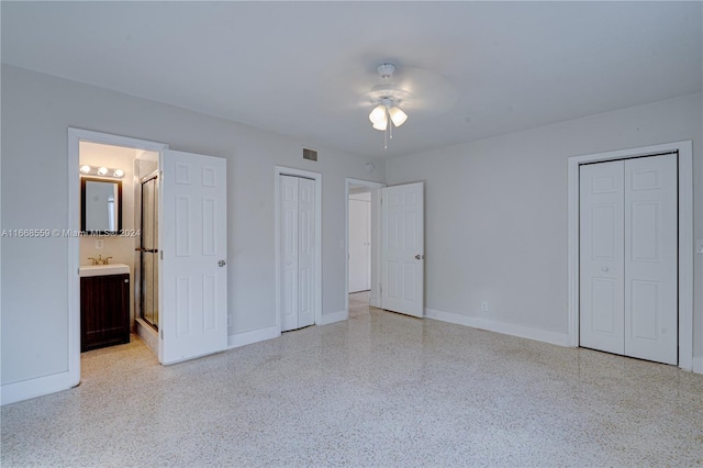 unfurnished bedroom with two closets, ensuite bathroom, ceiling fan, and sink