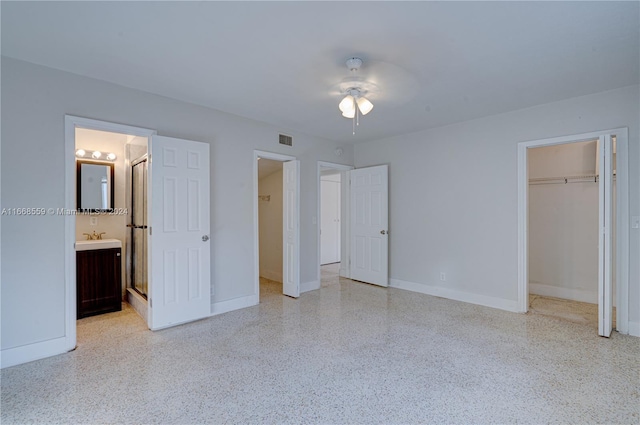 unfurnished bedroom featuring ensuite bathroom, a walk in closet, sink, ceiling fan, and a closet