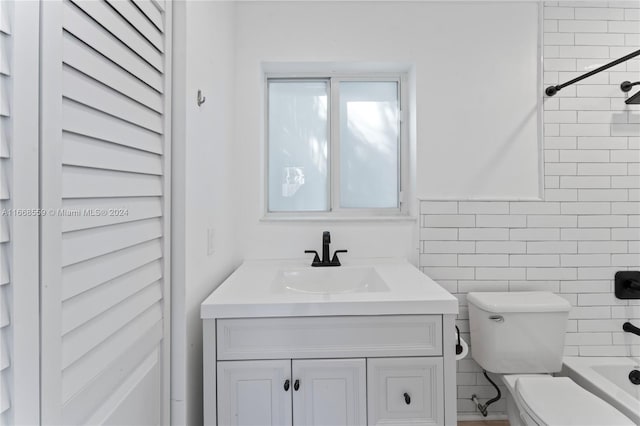 full bathroom featuring tiled shower / bath, vanity, tile walls, and toilet