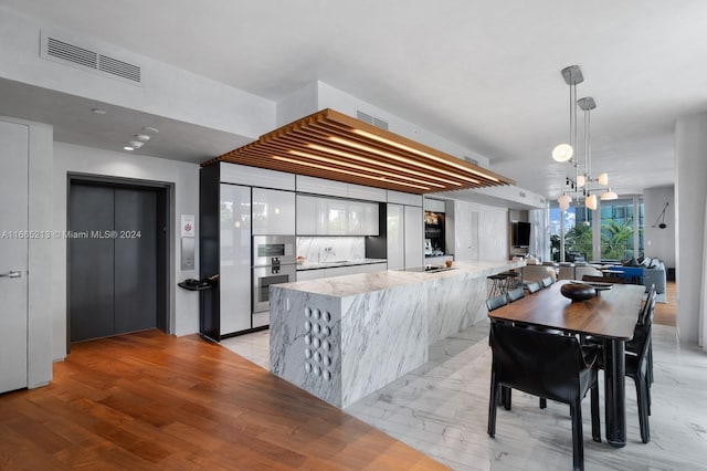 kitchen featuring light stone countertops, kitchen peninsula, pendant lighting, light hardwood / wood-style floors, and white cabinets