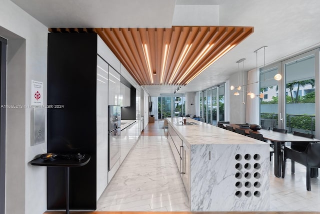 kitchen featuring light stone countertops, a large island with sink, decorative light fixtures, and plenty of natural light