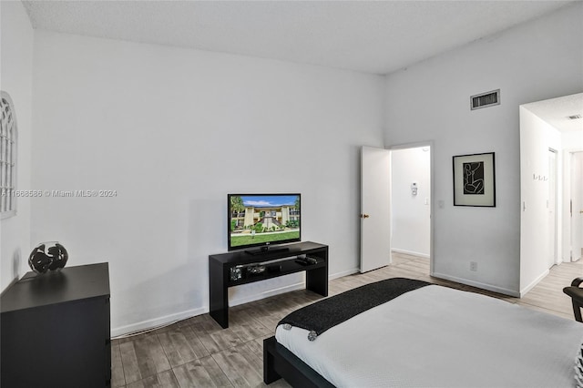 bedroom featuring a textured ceiling, a towering ceiling, and light hardwood / wood-style floors