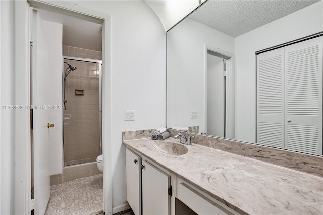 bathroom featuring a textured ceiling, a shower with shower door, vanity, and toilet