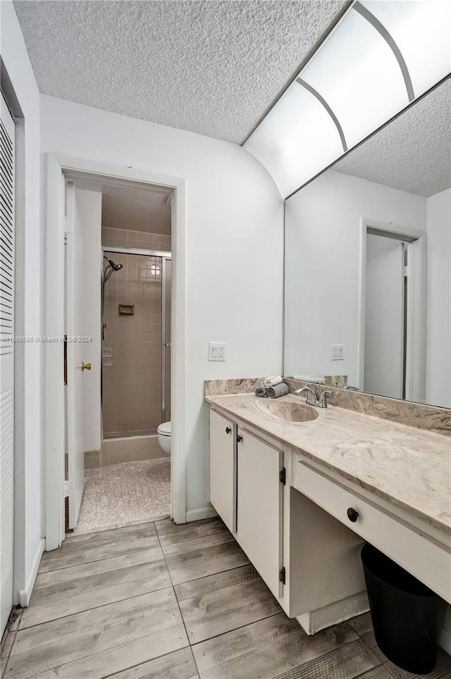 bathroom with vanity, a textured ceiling, hardwood / wood-style flooring, toilet, and a shower with door