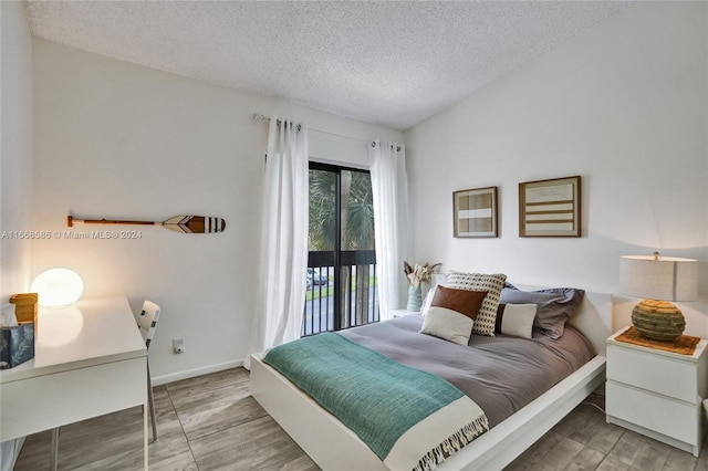 bedroom with light hardwood / wood-style flooring, vaulted ceiling, a textured ceiling, and access to exterior