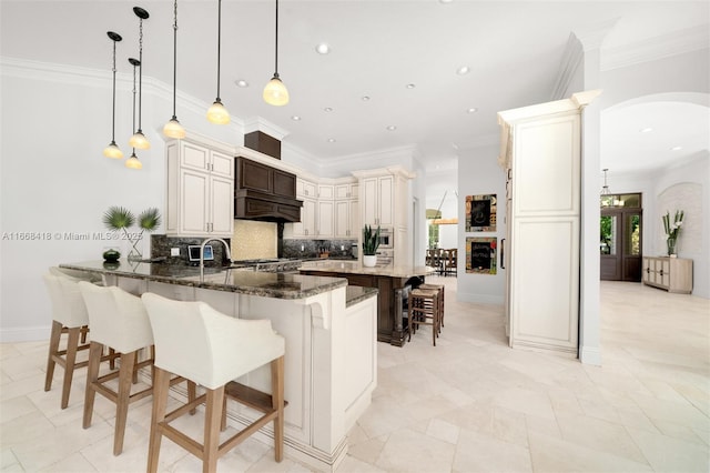 kitchen featuring pendant lighting, custom exhaust hood, a kitchen breakfast bar, dark stone countertops, and tasteful backsplash