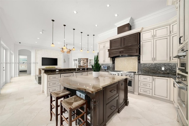 kitchen with dark stone countertops, high end stainless steel range, a kitchen island, and hanging light fixtures