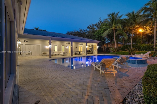 pool at dusk with outdoor lounge area, ceiling fan, a patio area, and an in ground hot tub