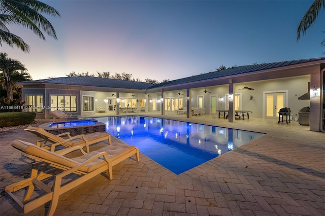 pool at dusk with ceiling fan, a patio area, an in ground hot tub, and french doors