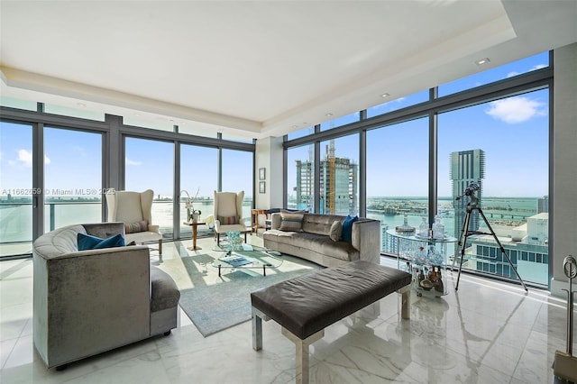 living room featuring a water view, expansive windows, a raised ceiling, and baseboard heating