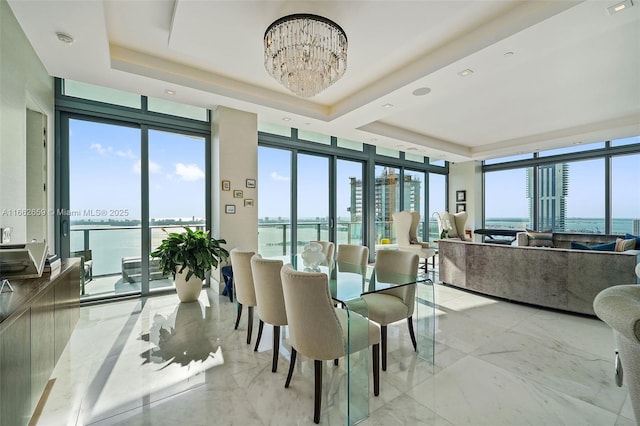 dining room with a wealth of natural light, a chandelier, a raised ceiling, floor to ceiling windows, and a water view