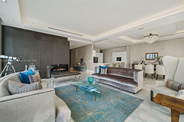 living room with an inviting chandelier, a large fireplace, and a raised ceiling