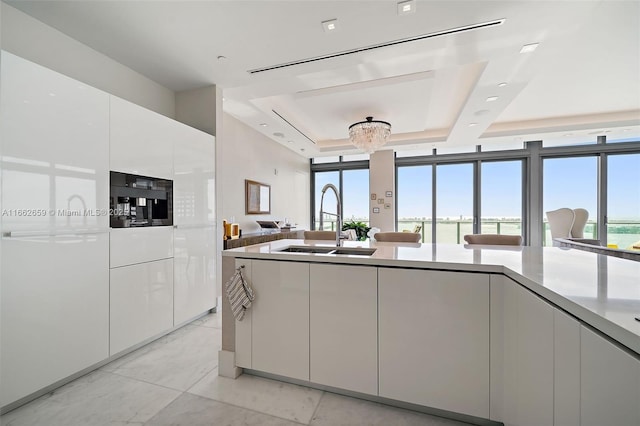 kitchen with sink, white cabinets, a wall of windows, a raised ceiling, and a water view