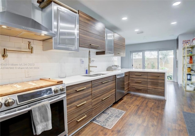 kitchen featuring wall chimney exhaust hood, tasteful backsplash, dark wood-type flooring, sink, and stainless steel appliances