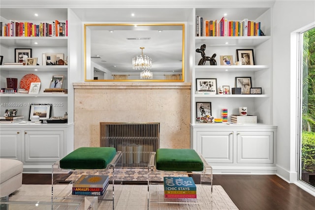 sitting room with built in features, wood finished floors, a premium fireplace, baseboards, and a chandelier