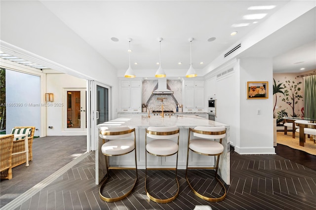 kitchen featuring light stone countertops, an island with sink, recessed lighting, white cabinets, and a kitchen breakfast bar