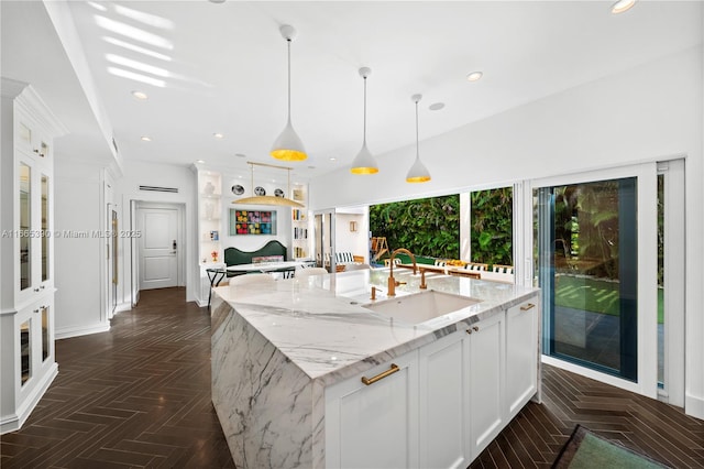 kitchen featuring a sink, recessed lighting, white cabinets, light stone countertops, and a large island with sink