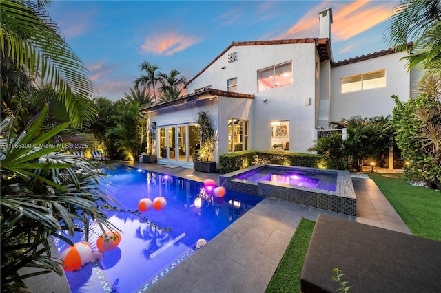 back of property with stucco siding, french doors, a patio area, an outdoor pool, and an in ground hot tub