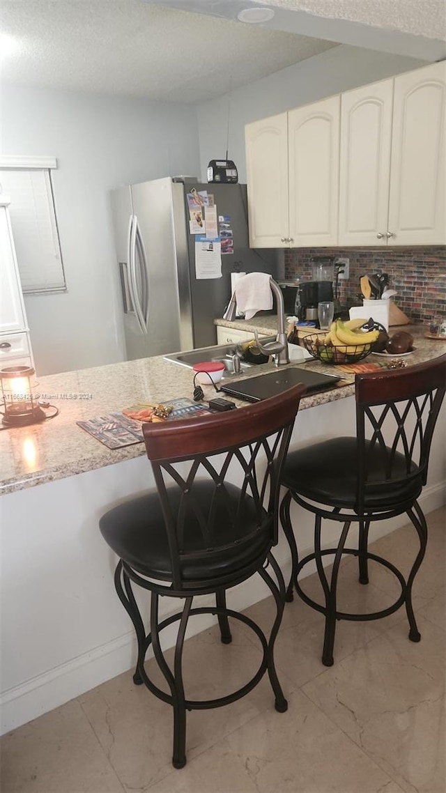 kitchen featuring decorative backsplash, stainless steel fridge, a kitchen bar, white cabinetry, and a textured ceiling