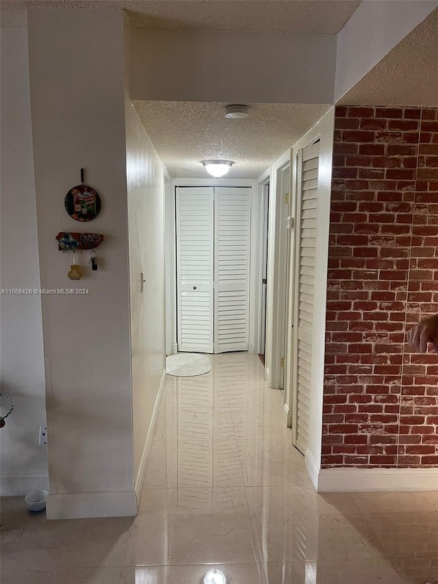 corridor featuring a textured ceiling and brick wall