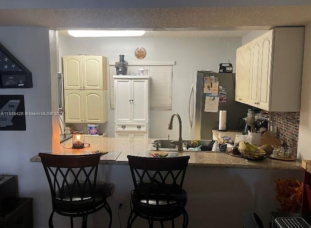 kitchen with kitchen peninsula, stainless steel fridge, white cabinets, tasteful backsplash, and a breakfast bar