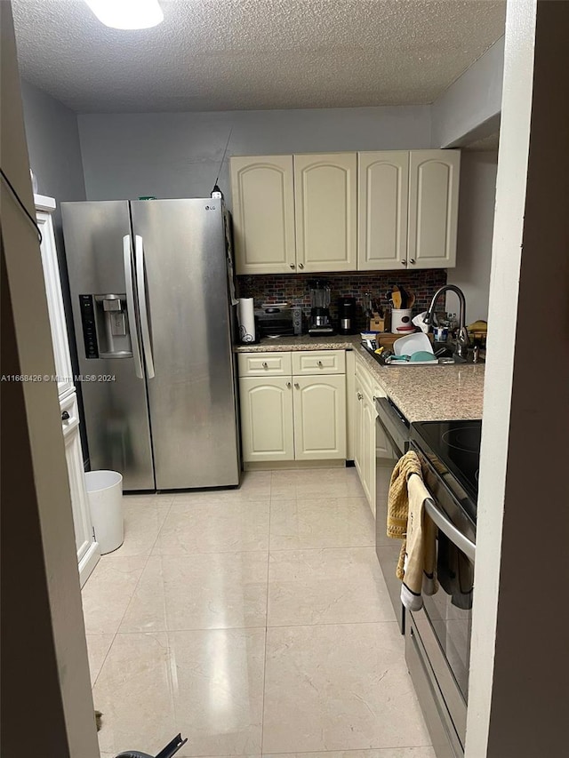 kitchen featuring cream cabinets, sink, a textured ceiling, stainless steel appliances, and decorative backsplash